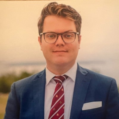 A man wearing a suit and tie and glasses looking at the camera.