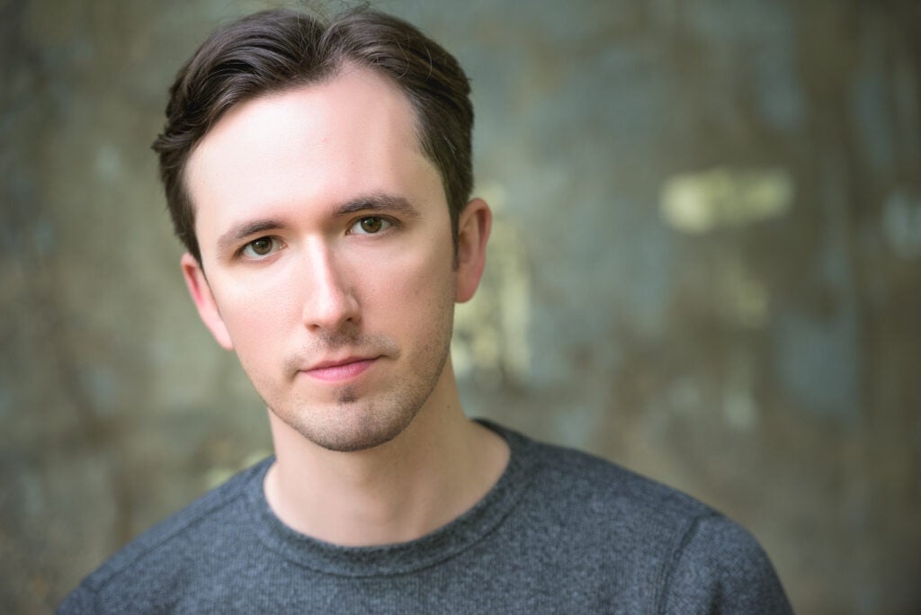 A headshot of a man wearing a gray shirt.