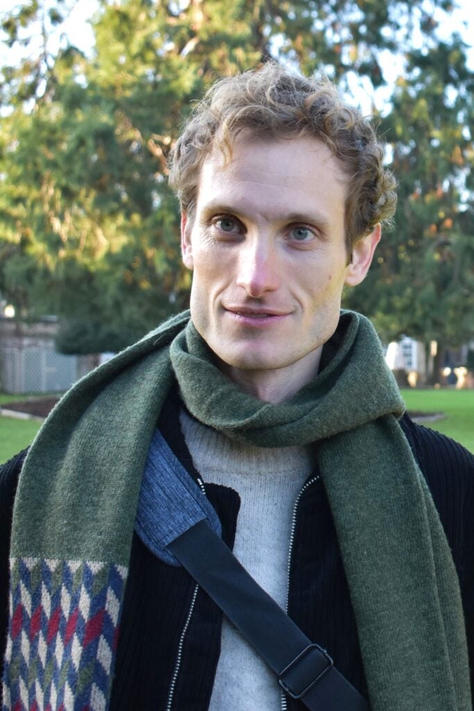 A man wearing a sweater and scarf smiling at the camera.