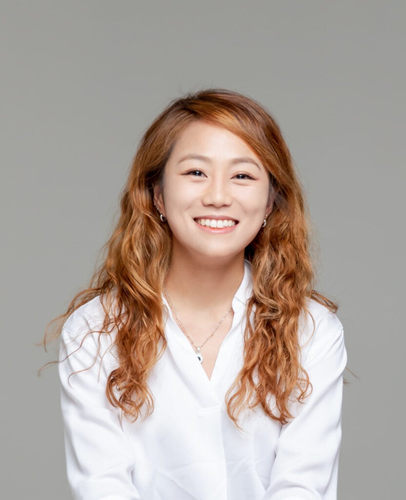 A woman wearing a white shirt smiling at camera for her headshot.