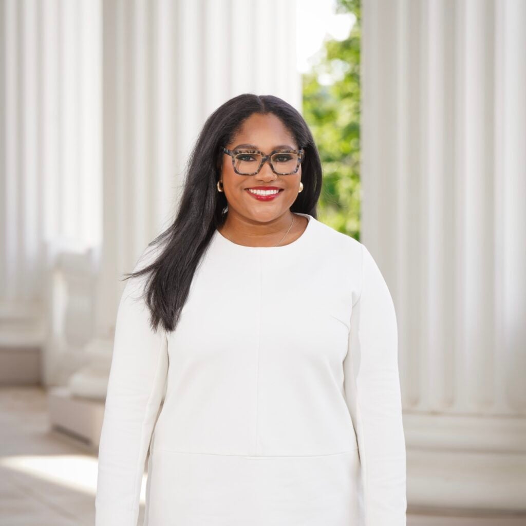 A woman wearing a white sweater and glasses smiling at the camera.
