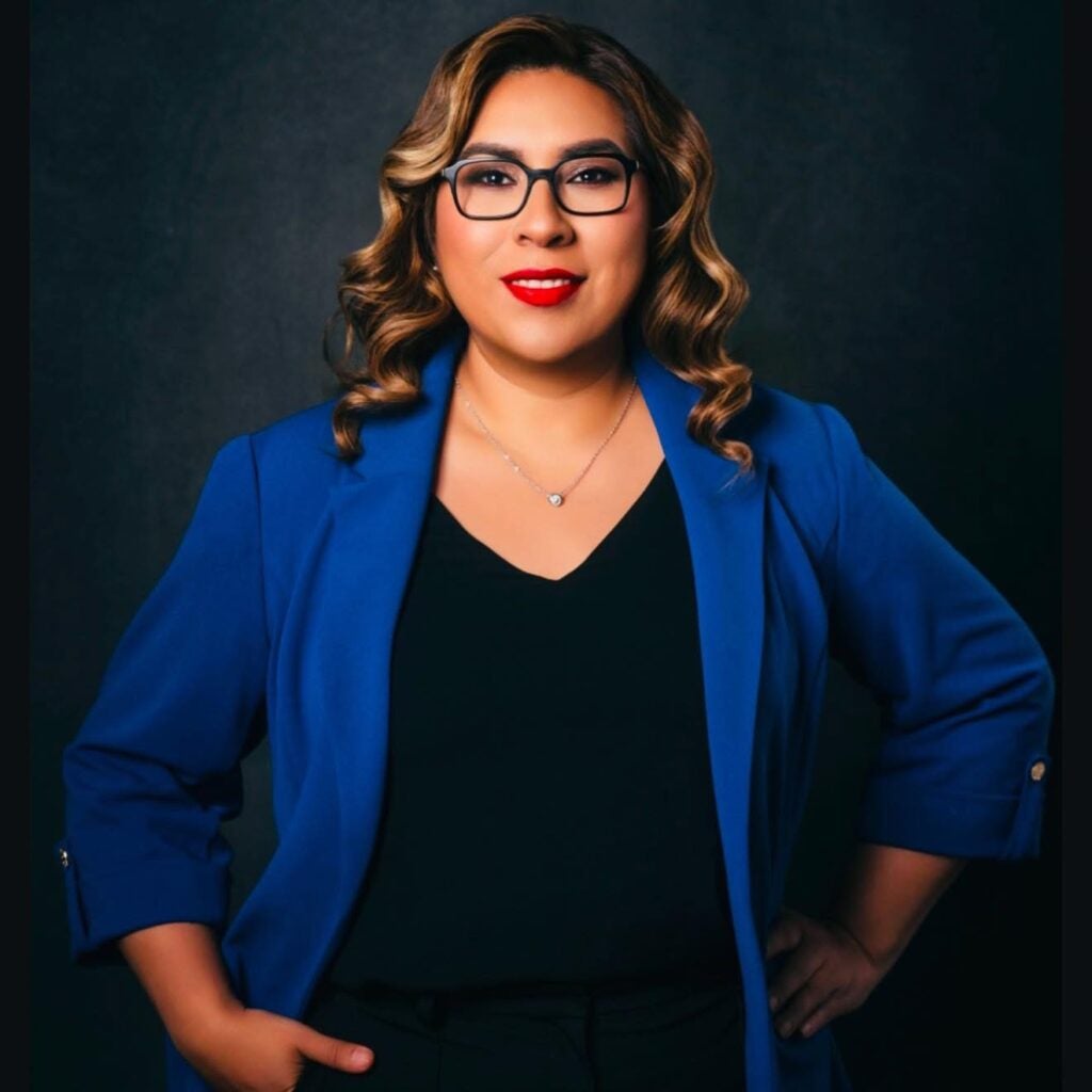 Portrait of a smiling woman in a black shirt and blue jacket.