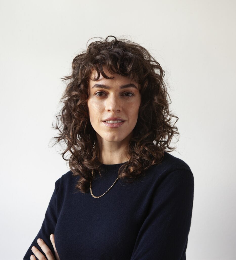 A woman wearing a sweater and a necklace smiling at the camera.