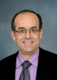 Headshot of smiling man wearing a purple shirt, polka dot tie and black jacket