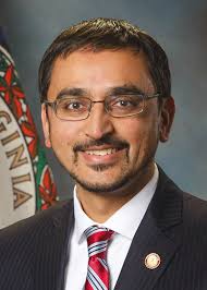 A man with glasses wearing a suit and red and blue tie smiling for a headshot.