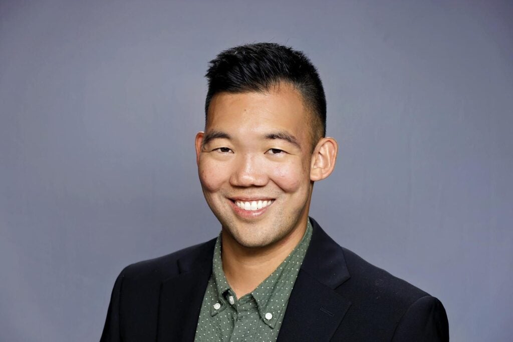 Headshot of a man wearing a black jacket and green dotted shirt