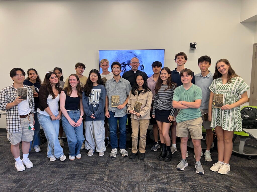 A group of students stand together during class, smiling and holding up their books.