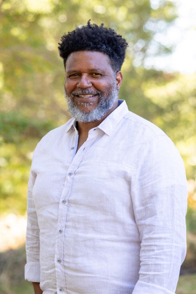 A professor wearing a light-colored buttoned dress shirt and smiling.