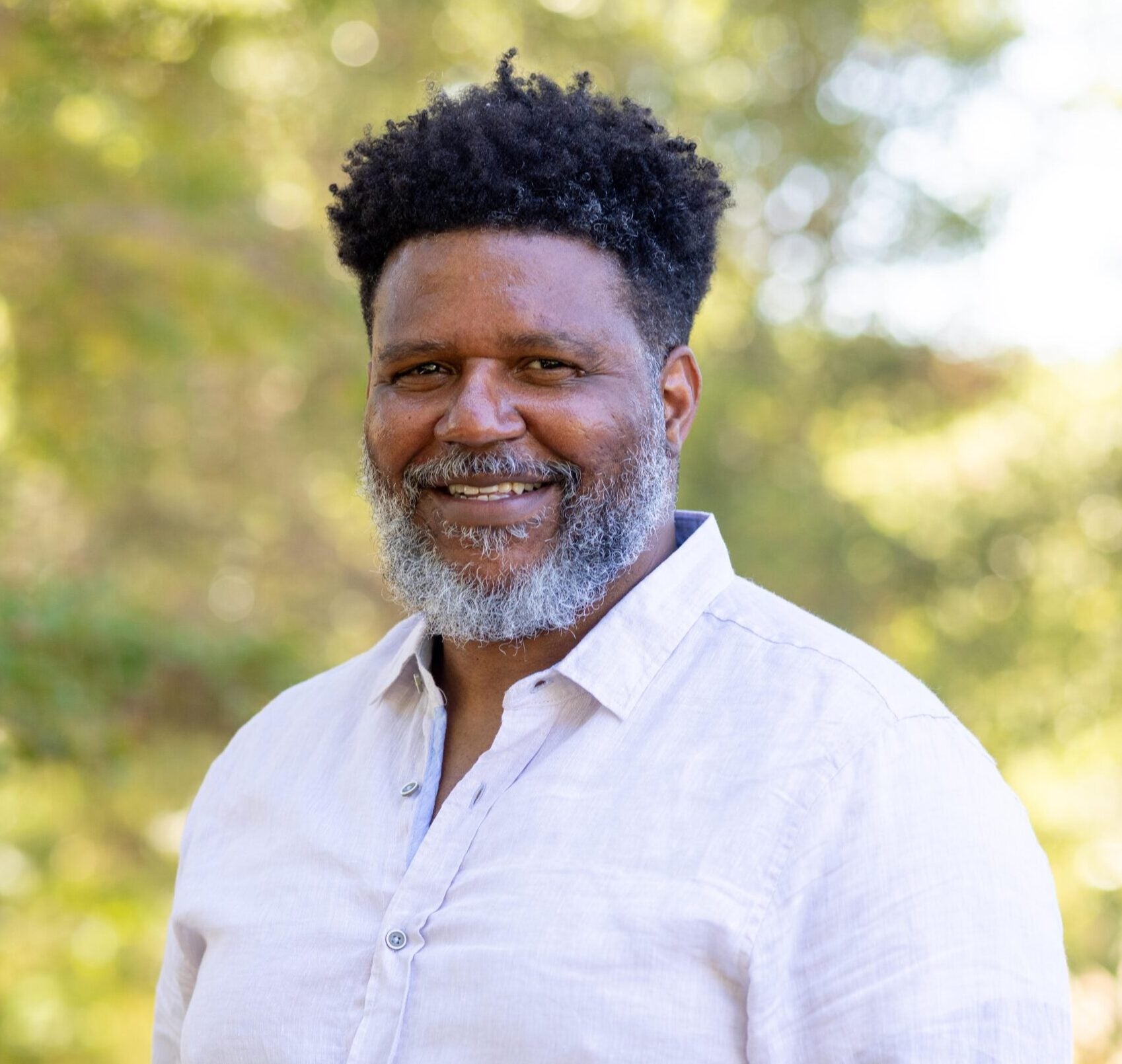 A professor wearing a light-colored button-down dress shirt and smiling