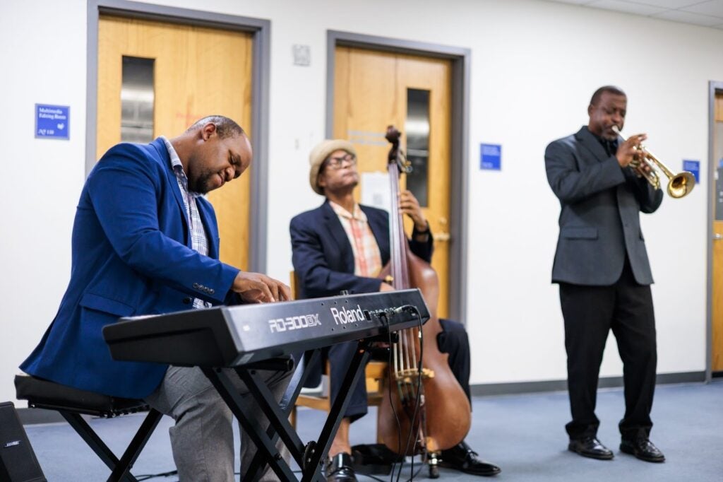A trio of jazz musicians performs at the reception, with a pianist, bassist, and trumpet player entertaining guests in a warmly lit room.