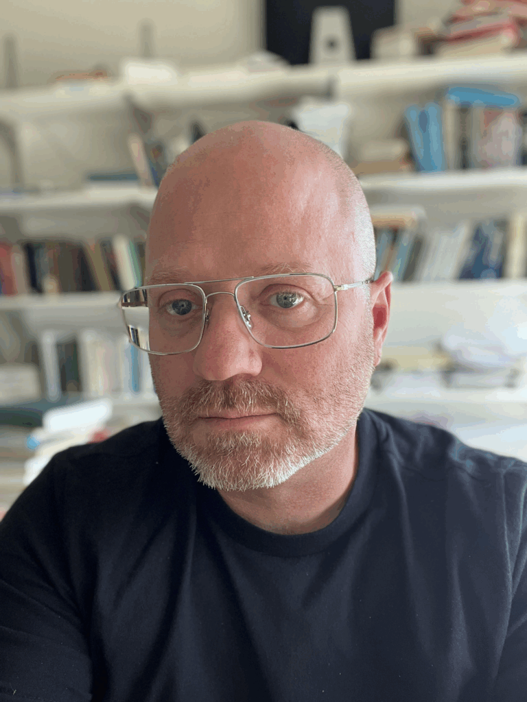 A headshot of a professor wearing glasses and wearing a dark T-shirt