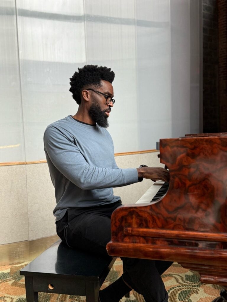 A professor wearing a sweater and glasses playing the piano