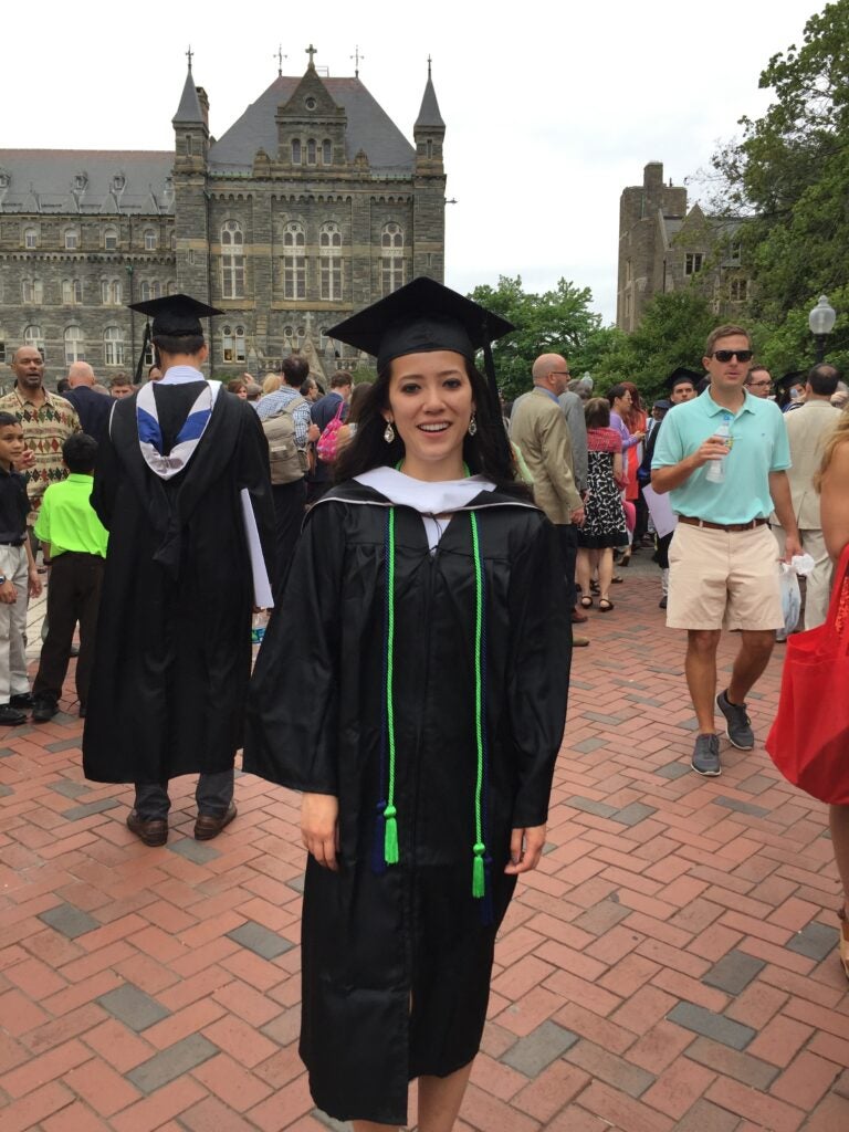 A Georgetown University graduate wearing a cap and gown standing in front of Healy Hall