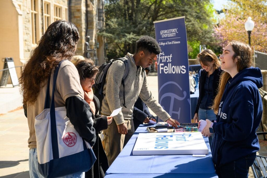 A group of Georgetown students standing near a table during an event with staff and faculty members on the other side.