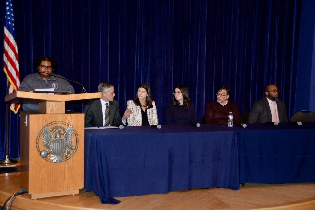 A moderator standing behind a podium and a five panelists sitting behind a table for an event at Georgetown University