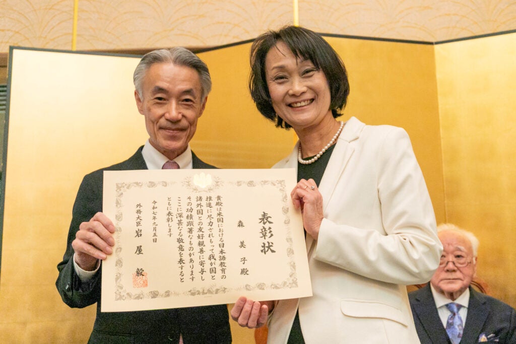 A professor and an ambassador hold a commendation award.