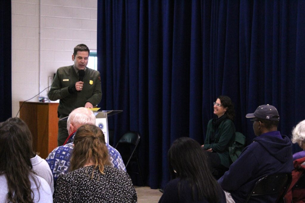 A park ranger standing and speaking to a group of people at a symposium.