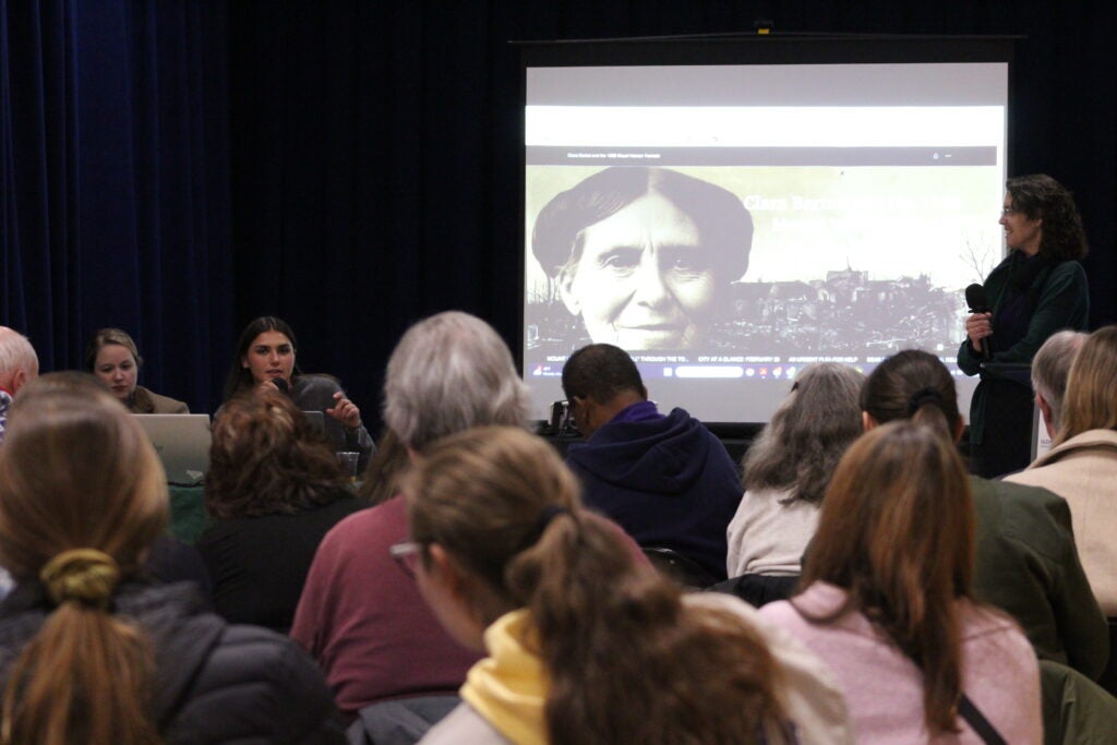A student giving her presentation at a symposium in front of a crowd.