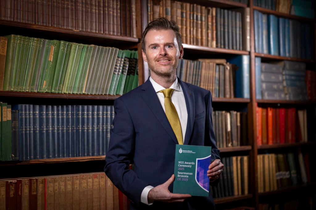 A professor wearing a suit and tie holding an awards ceremony pamphlet.