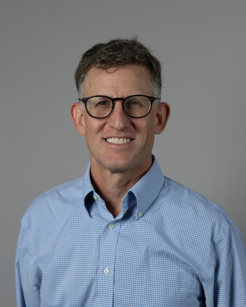 A male professor wearing a checkered shirt and glasses smiling.