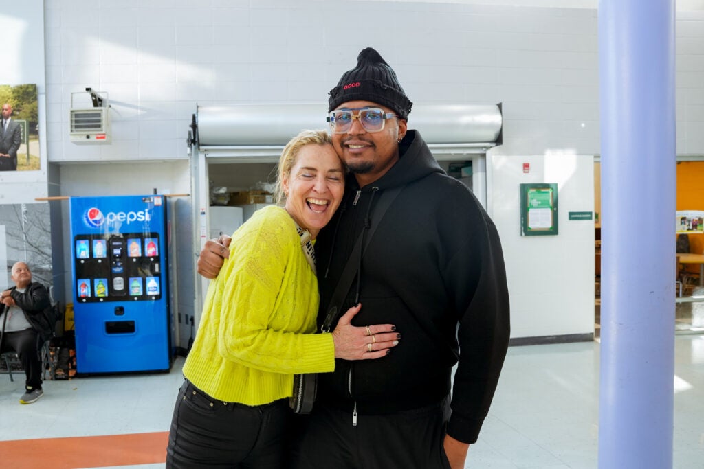 Two friends, a woman in a yellow sweater and a man in a black hoodie and glasses share an embrace