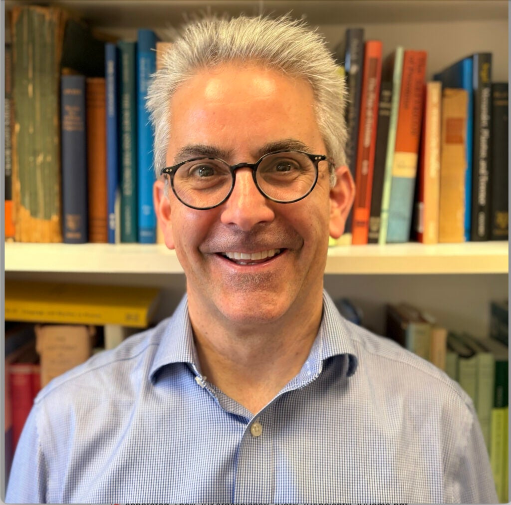 A professor of Classics wearing a dress shirt and glasses smiling