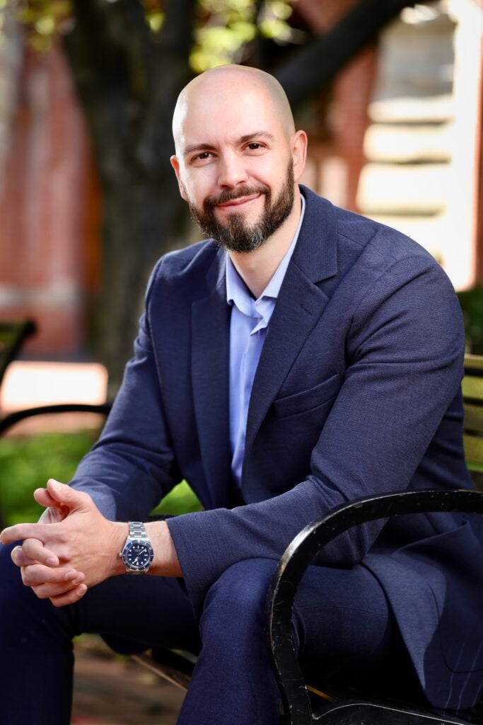 A history professor wearing a suit jacket and shirt and sitting down on a bench smiling