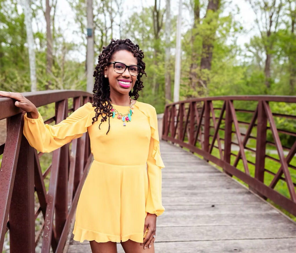A professor wearing a yellow dress and a colorful necklace posing on a bridge