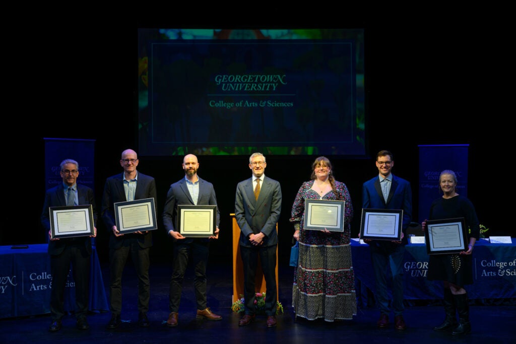 A dean and group of Georgetown University professors and staff members standing with their awards