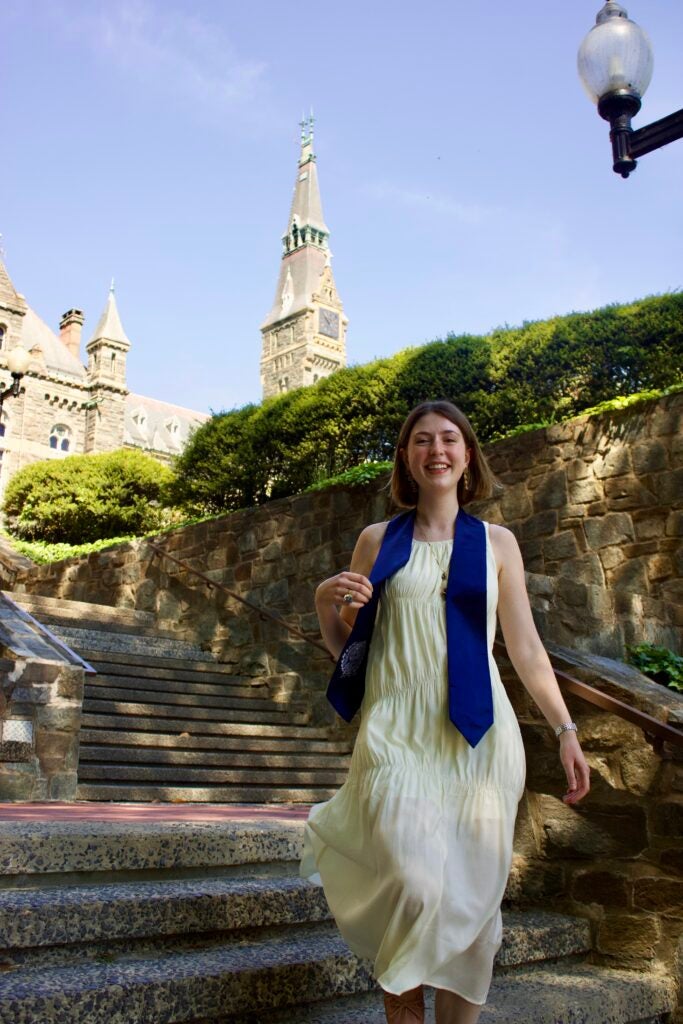 A graduating senior walking down steps in front of Healy Hall at Georgetown