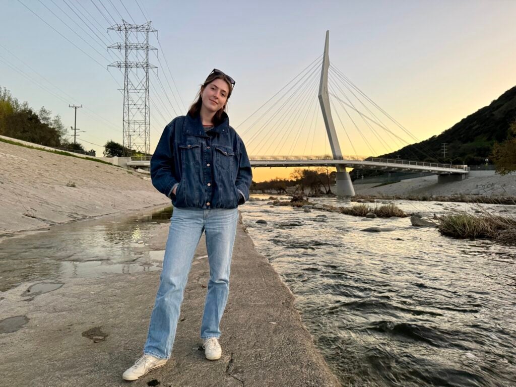 A Georgetown student wearing a jean jacket and jeans standing next to the Los Angeles River