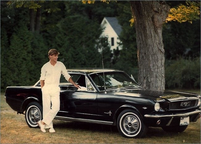 A young man standing next to his 1965 Ford Mustang