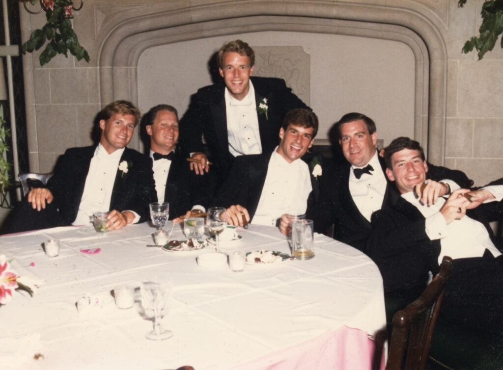 Men wearing tuxedos sitting a table together during a wedding