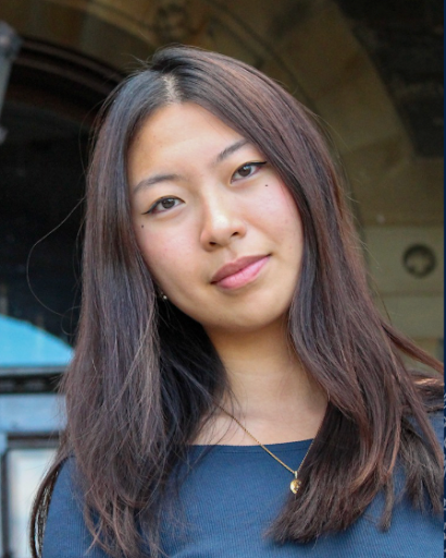 A student wearing gray in front of a blurred building in the background.