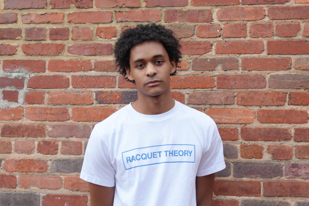 A Georgetown alum wearing a white T-shirt with the words "Racquet Theory" printed on the front.
