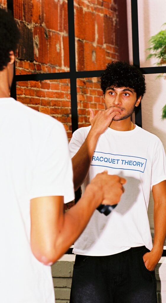 A Georgetown graduate wearing a "Racquet Theory" T-shirt staring off to the side with his hand near his face.