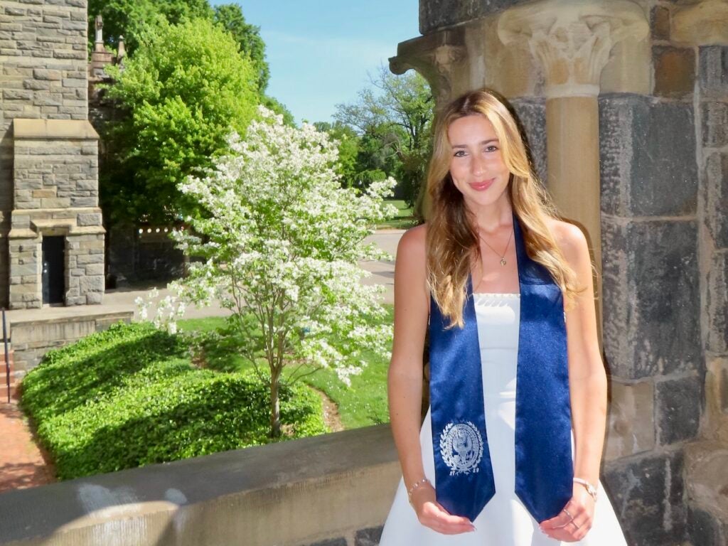 A woman in a white dress and Georgetown graduation sash posing on campus.
