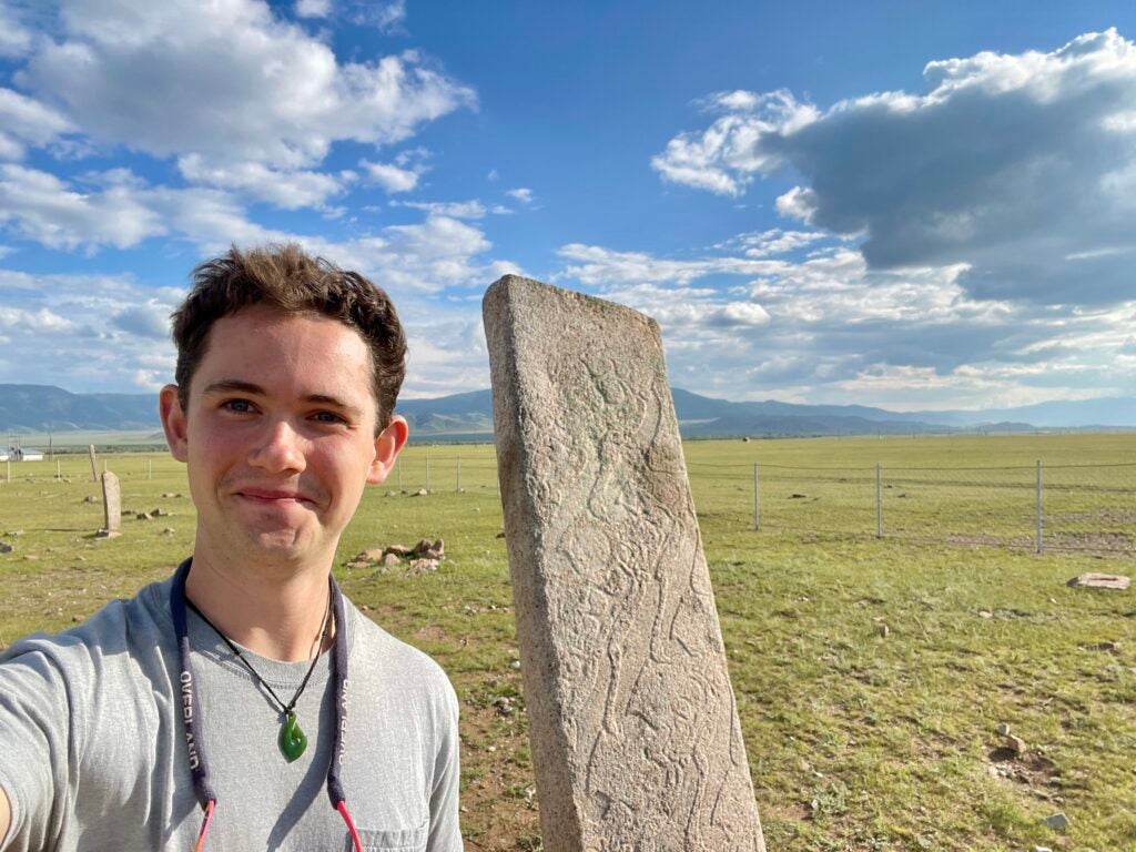 A man wearing a gray shirt posing in front of a stone monument.
