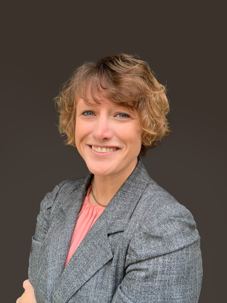 Headshot of a Georgetown University professor smiling in front of a gray background.