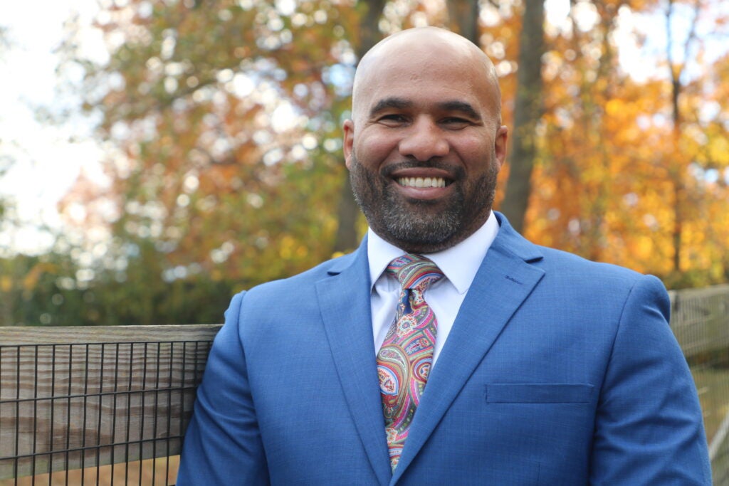 Headshot of a Georgetown University administrator smiling and wearing a suit and tie in front of a blurred nature background.