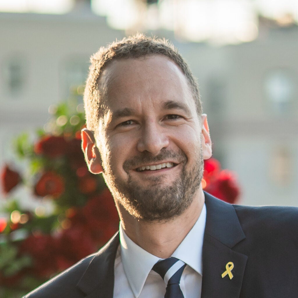Headshot of a Georgetown University visiting professor smiling in front of a blurred background.