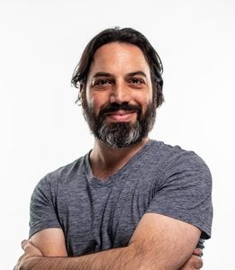 A headshot of a Georgetown University professor smiling with his arms crossed.
